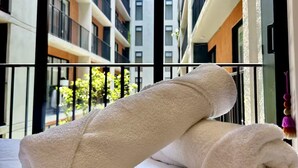 Een bed met twee opgerolde handdoeken en uitzicht op een modern gebouw met balkons.
