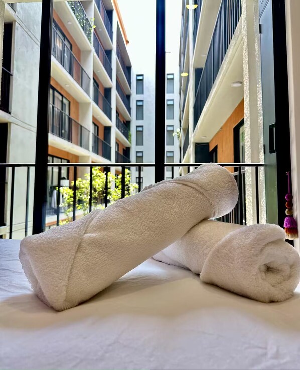 A bed with two rolled towels and a view of a modern building with balconies.