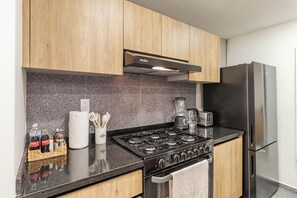 A modern kitchen with wooden cabinets, a gas stove, a stainless steel refrigerator, and a granite countertop.