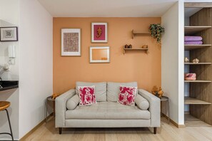Una sala de estar con sofá, una obra de arte enmarcada, un estante con adornos y una planta.