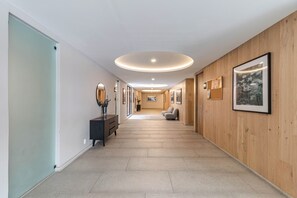 A hallway with a wooden wall, a black bench, and a mirror on the left.