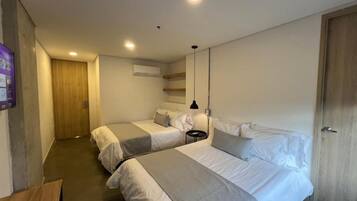 A hotel room with two beds, a wooden door, a small table, and a ceiling light.