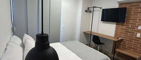 Una habitación de hotel moderna con una cama, un escritorio, una silla, un televisor montado en la pared y una lámpara colgante.