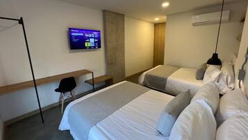 A hotel room with two beds, a desk, a chair, a TV mounted on the wall, and an air conditioning unit.
