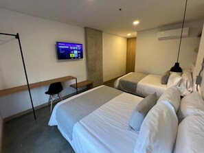 Une chambre d’hôtel avec deux lits, un bureau, une chaise, un téléviseur fixé au mur et un appareil de climatisation.