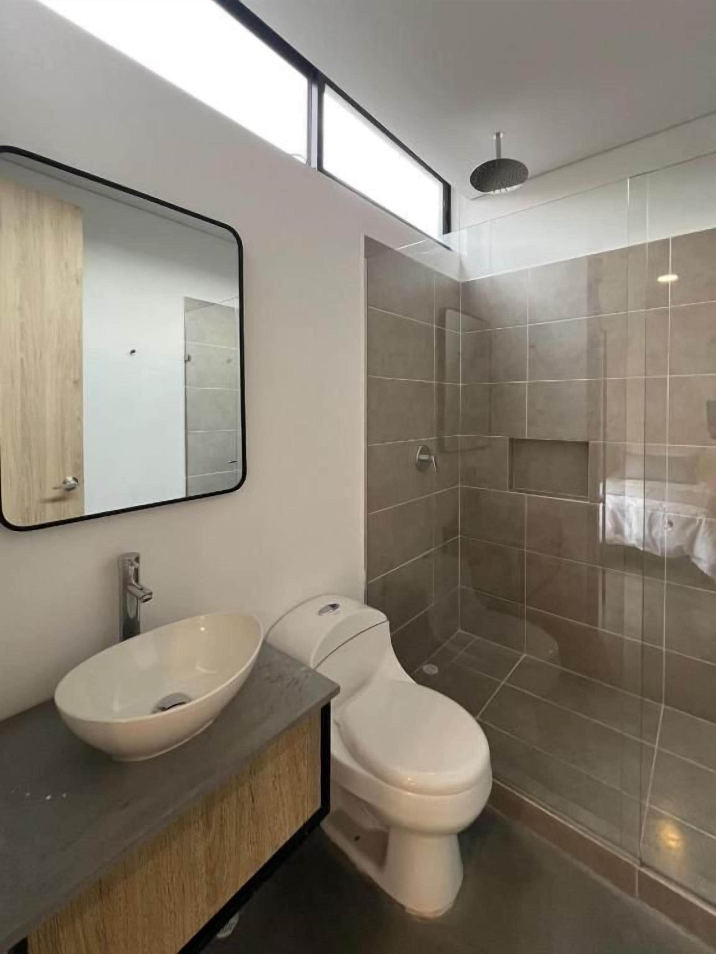 A modern bathroom with a large mirror, a vessel sink, a toilet, and a glass-enclosed shower.