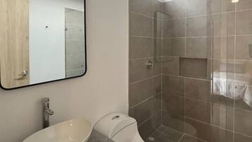 A modern bathroom with a large mirror, a vessel sink, a toilet, and a glass-enclosed shower.