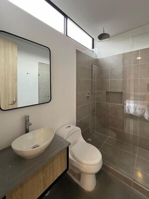 Une salle de bain moderne avec un grand miroir, un lavabo sur colonne, des toilettes et une douche à parois de verre.