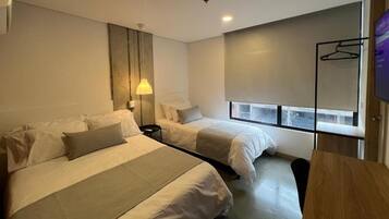 Una camera d'albergo con due letti, un comodino, una lampada, un televisore e una finestra con vista.