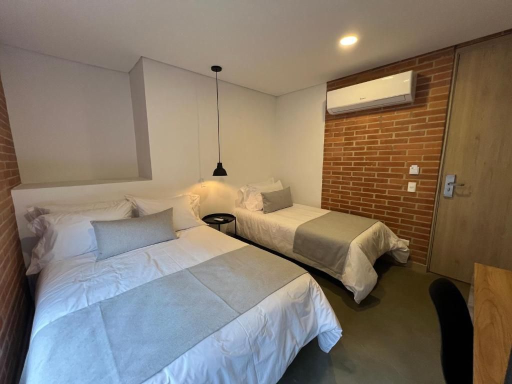 A hotel room with two beds, a small table, a hanging light, and a brick wall.