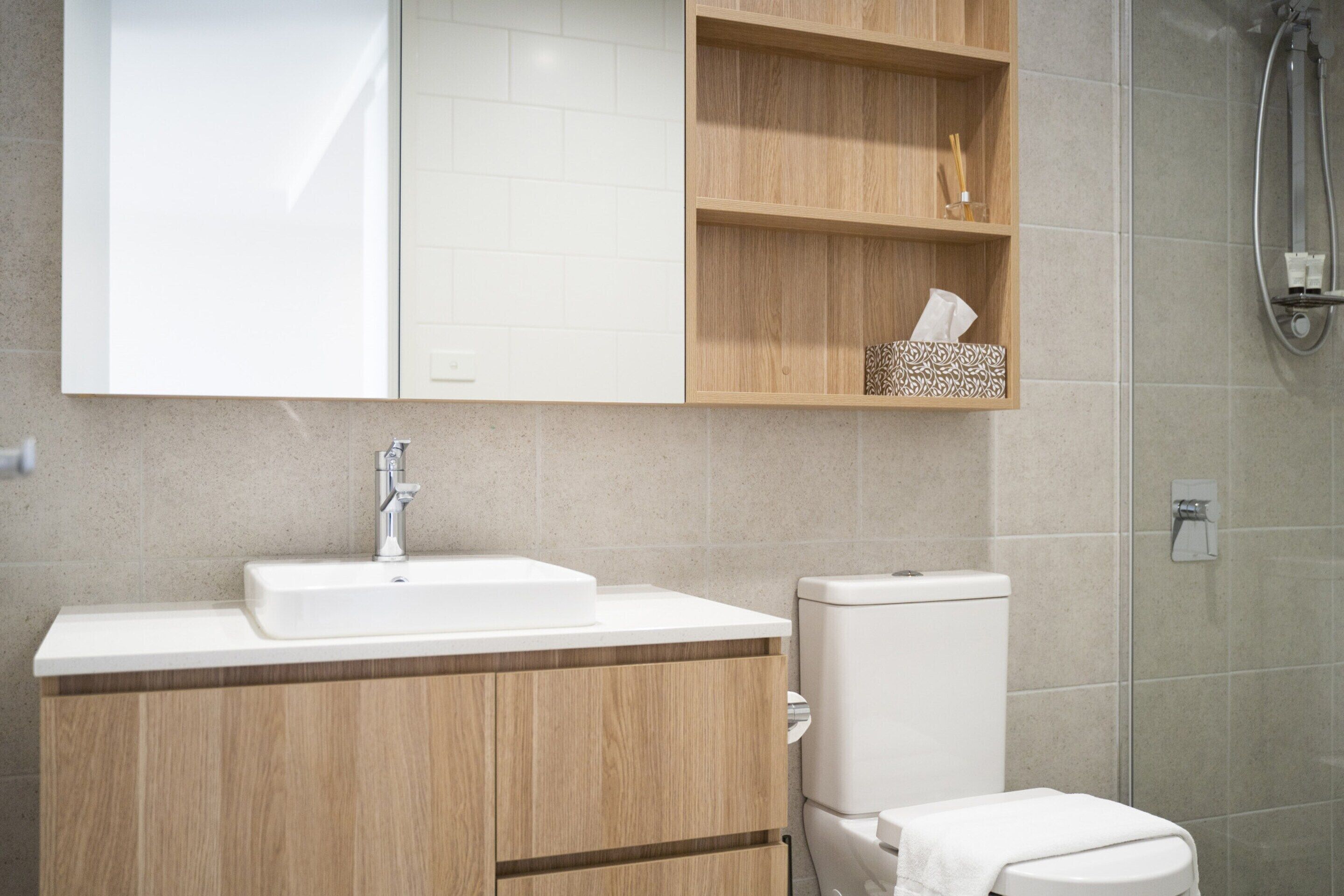 Un baño moderno con tocador de madera, lavamanos blanco y retrete.