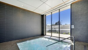 Uma piscina interior moderna com paredes de vidro transparente, uma escada de metal e vista para o exterior.