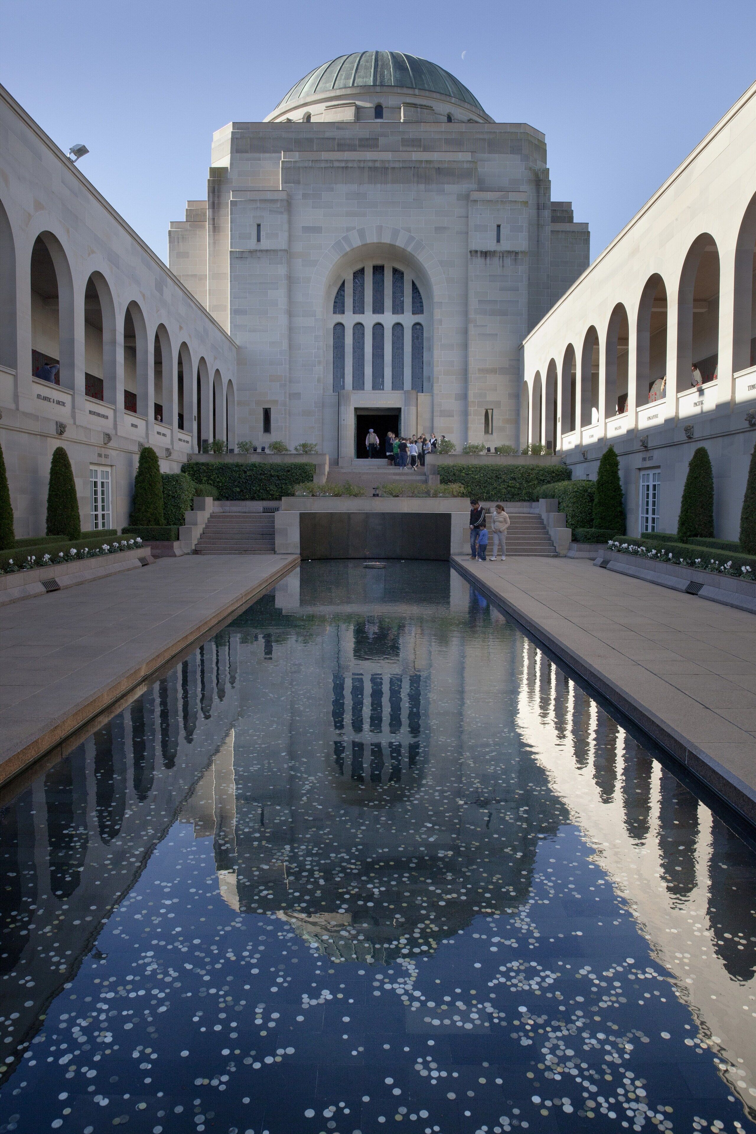 A large building with a central dome and arched windows, surrounded by a reflective pool with floating objects.