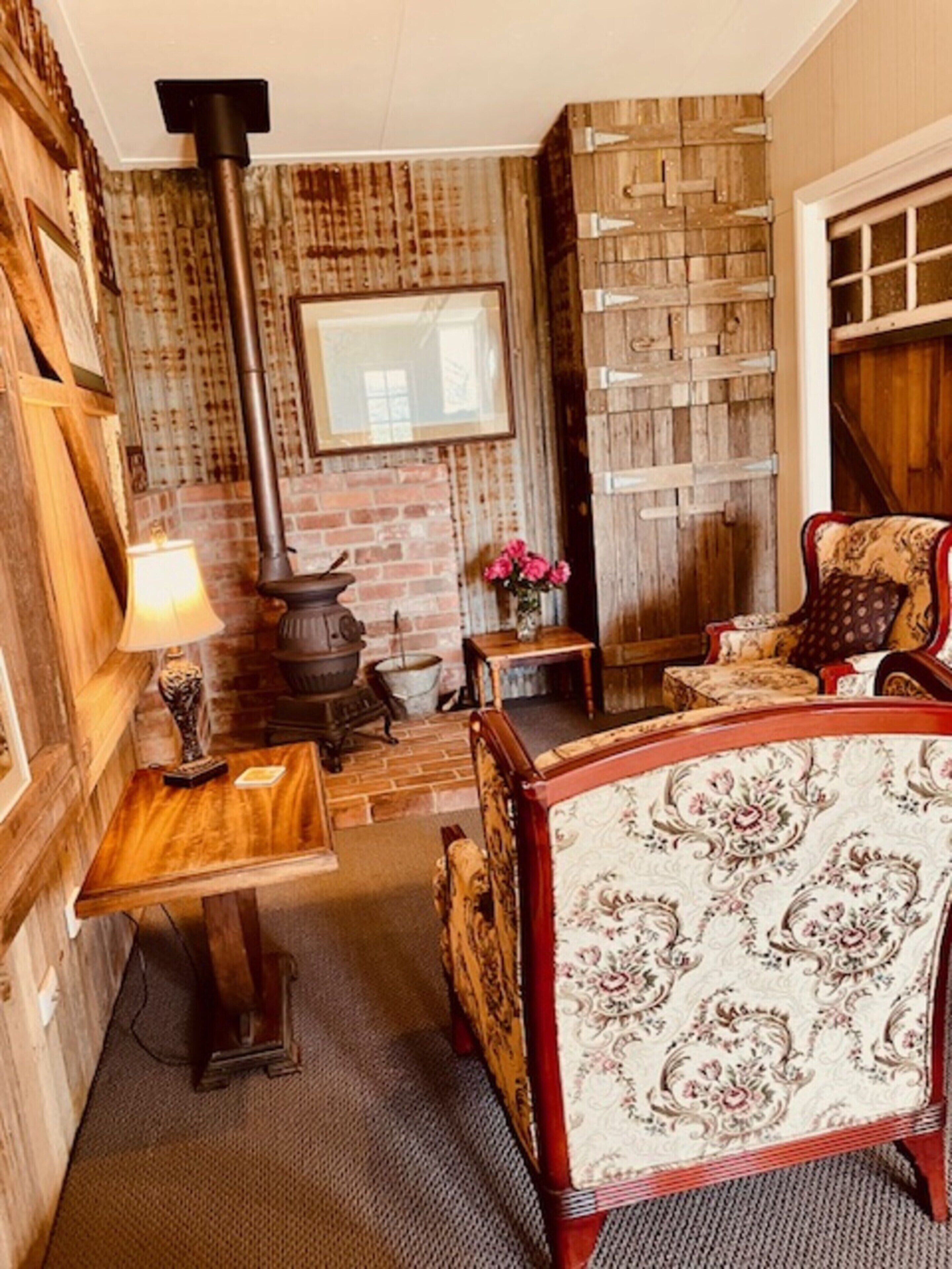 A cozy room with a brick fireplace, a wooden table, a patterned armchair, and a mirror on the wall.