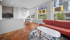 A modern living room with a herringbone wood floor, a red sofa, a white coffee table, and large windows offering views of the city. - Chic 1-bed Apartment In the Heart of Melbourne (Melbourne)