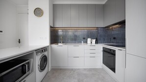 A modern kitchen with a washing machine, microwave, oven, and a clock on the wall. - Chic 1-bed Apartment In the Heart of Melbourne (Melbourne)