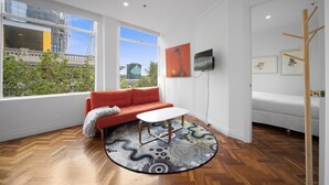 A modern living room with a wooden herringbone floor, a red sofa, a white coffee table, and a round rug. - Chic 1-bed Apartment In the Heart of Melbourne (Melbourne)