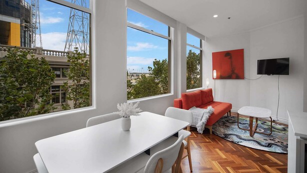 A modern living room with a white sofa, a red accent sofa, a white dining table, and a TV mounted on the wall. - Chic 1-bed Apartment In the Heart of Melbourne (Melbourne)