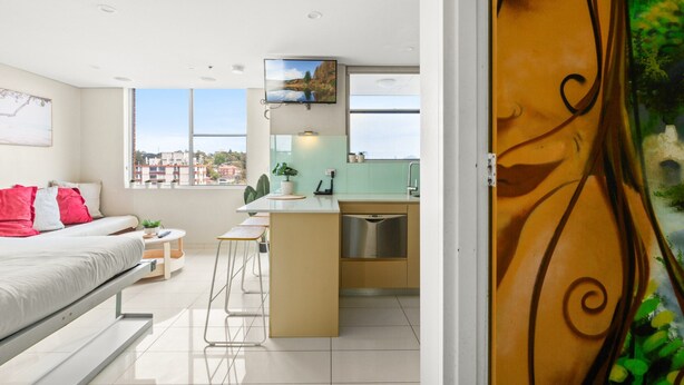 Ein modernes Apartment mit Schlafzimmer, Küchenzeile und einem großen Fenster mit Blick auf die Stadt.