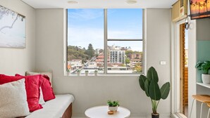 Ein modernes Zimmer mit großem Fenster, einer Couch mit roten Kissen, einem kleinen Tisch mit Pflanze und einem Blumentopf in der Nähe des Fensters.