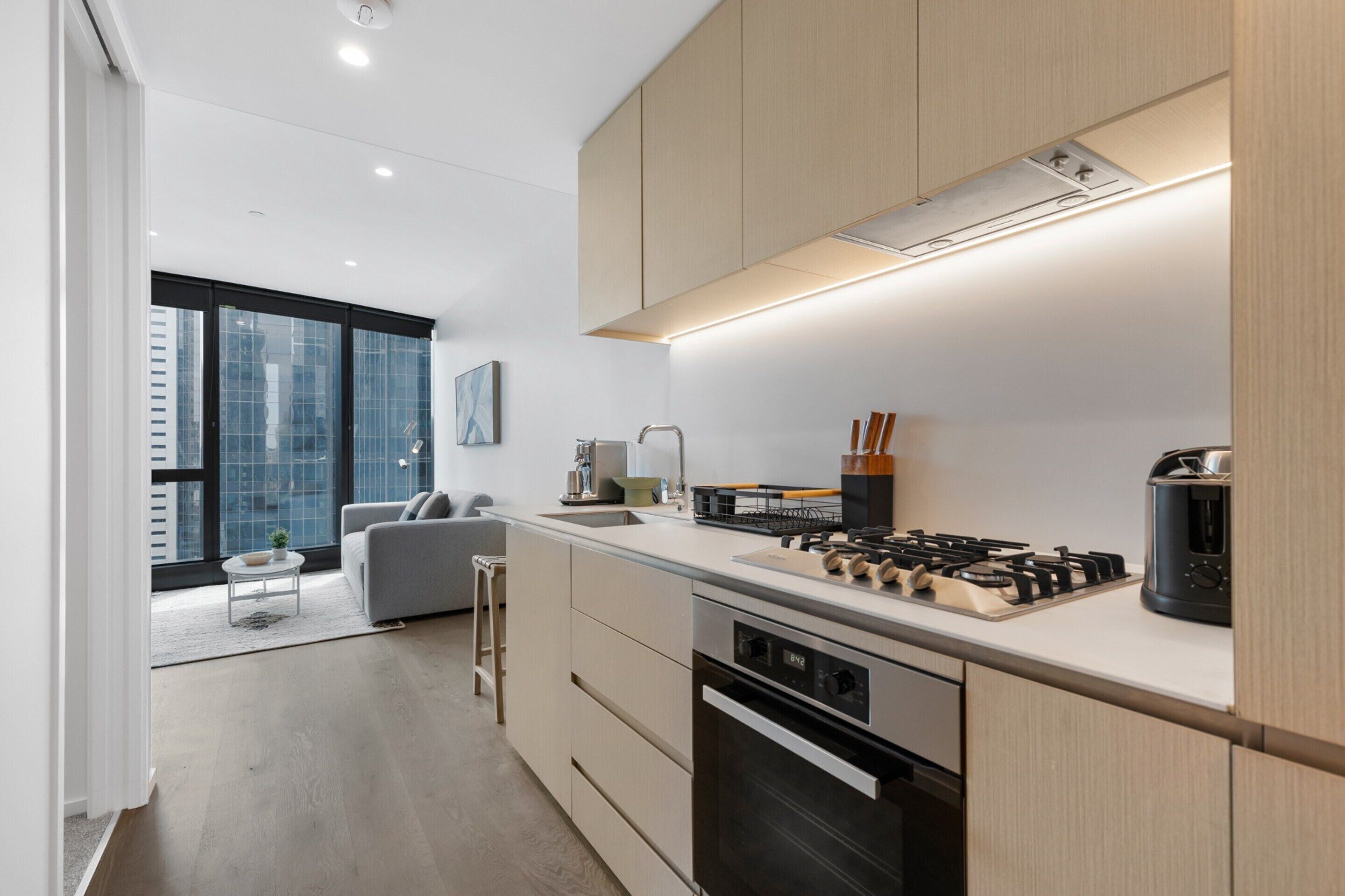 A modern kitchen with a built-in stove, oven, and sink. There is a dining area with a gray sofa and a small table.