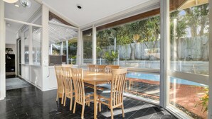 A dining area with a glass-enclosed patio, a pool, and a view of the backyard. - 5-bed Haven With Pool Minutes From Beaches (Melbourne)