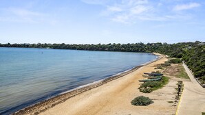 A beach with clear blue water, a sandy shore, and several boats lined up along the edge. - 5-bed Haven With Pool Minutes From Beaches (Melbourne)