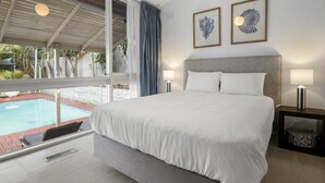 A bedroom with a large bed, two bedside lamps, and a view of a swimming pool. - 5-bed Haven With Pool Minutes From Beaches (Melbourne)