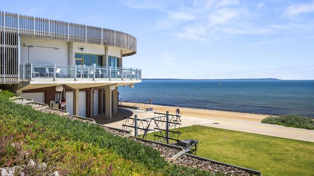 A modern coastal building with a balcony overlooking the sea, a basketball court, and a grassy area. - 5-bed Haven With Pool Minutes From Beaches (Melbourne)
