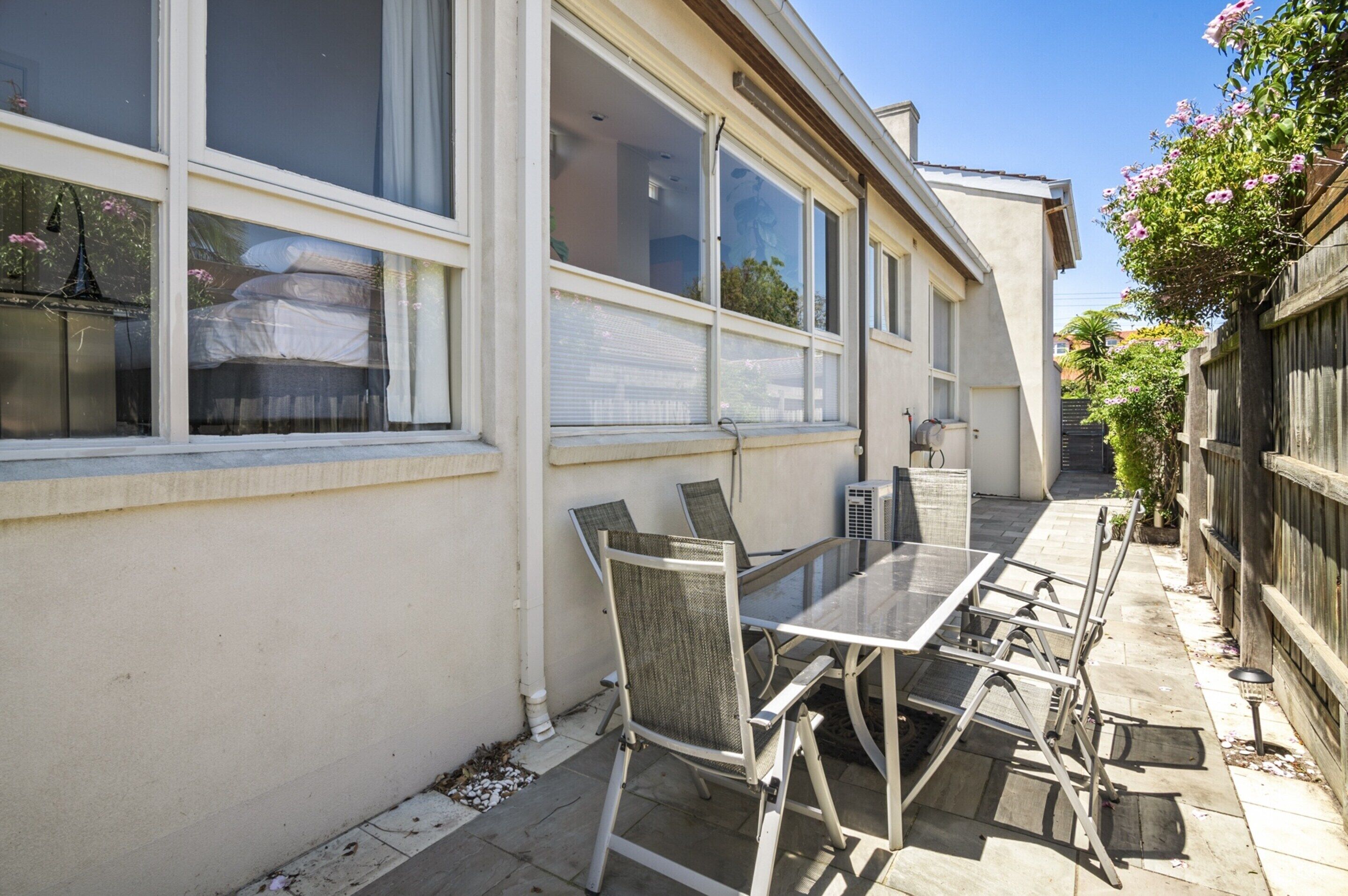 Une terrasse extérieure avec une table et des chaises, de grandes fenêtres et une clôture en bois.