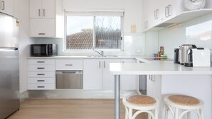 A modern kitchen with white cabinets, stainless steel appliances, a window, and a clock on the wall.