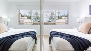 A mirrored room with two beds, a large window, and a view of trees and buildings.