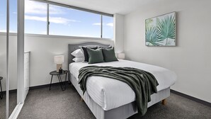 A modern hotel room with a large bed, a small bedside table with a lamp, and a window with a view of the sky. - Stunning Ocean Views With Manly At Your Doorstep (Sydney)