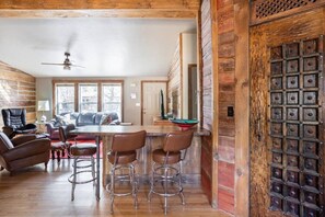 A rustic interior with a wooden dining area, bar stools, and a large wooden door with a grid pattern. - Cute cabin ideally located in Moab, Month rental (Moab)