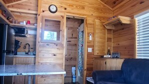 A wooden cabin interior with a kitchen area, a dining table, a sofa, and a ceiling fan. - Christopher Creek Cabins - Cabin 2 (Christopher Creek)
