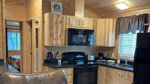 A cozy cabin interior with wooden walls, a kitchen area including a stove, microwave, and refrigerator, and a leather chair. - Christopher Creek Cabins - Cabin 2 (Christopher Creek)