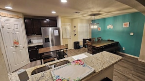 Una cocina con armarios oscuros, un refrigerador de acero inoxidable, una mesa de comedor de madera y una pared de acento color turquesa.