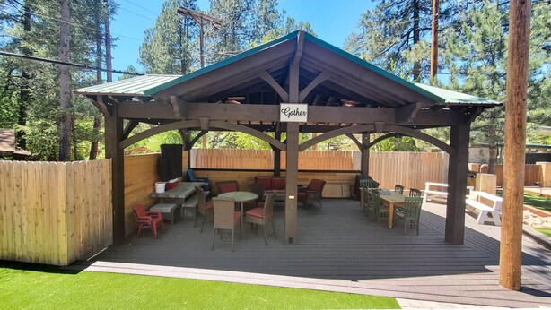 Un espace extérieur abrité, aménagé avec des tables et des chaises, une enseigne indiquant « Rassemblement », et une terrasse en bois.