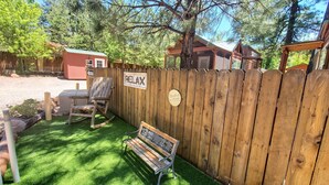 Une clôture en bois avec une pancarte indiquant « Détendez-vous », une chaise berçante et un banc dans un jardin avec une pelouse artificielle.