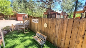 Une clôture en bois avec une pancarte indiquant « Détendez-vous », une chaise berçante et un banc dans un jardin avec une pelouse artificielle.