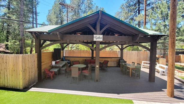 Un espace extérieur abrité, aménagé avec des tables et des chaises, une enseigne indiquant « Rassemblement », et une terrasse en bois.