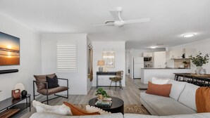 Una sala de estar moderna con un sofá, una mesa de centro y un sillón. Se observa un comedor con una mesa y sillas. Se ve una cocina al fondo.