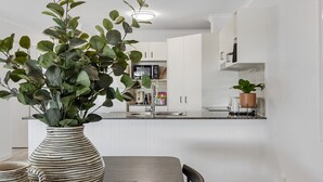 Una cocina moderna con armarios blancos, una mesa de comedor con sillas y una planta en maceta sobre la encimera.
