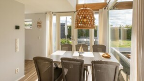 Un espace repas comprenant une table et des chaises, de grandes fenêtres et un luminaire au plafond.