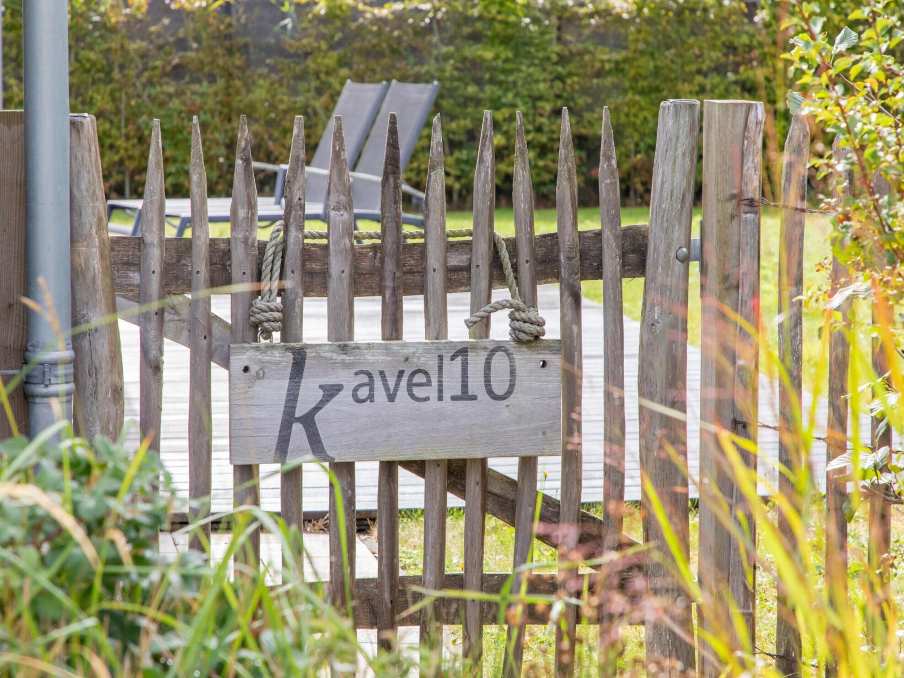 A wooden gate with a sign reading "KAVEL10" in a garden setting.