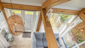 Un salon moderne avec un canapé gris, des poutres en bois, de grandes fenêtres et des lampes suspendues en osier.