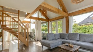 Un vaste espace de vie agrémenté d’un escalier en bois, d’un canapé d  ’angle gris et d’une table basse au style rustique.