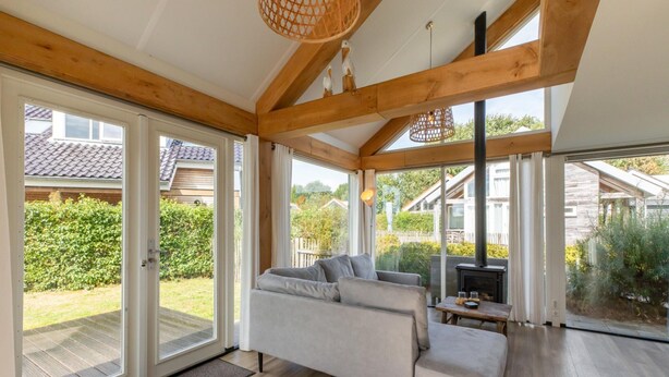 Un salon moderne avec un canapé, des poutres en bois, de grandes fenêtres et une vue sur l’extérieur.