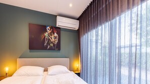 A hotel room with a bed, two bedside lamps, a painting on the wall, and an air conditioning unit. - Modern Chalet Near Beach in Renesse (Renesse)