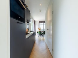 Una cocina moderna con estufa integrada, un comedor con mesa y sillas, y vistas al exterior a través de amplios ventanales.